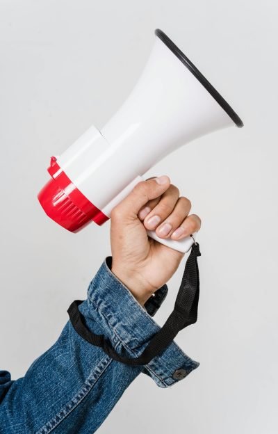 A person in a denim jacket holds a red and white megaphone, emphasizing communication.