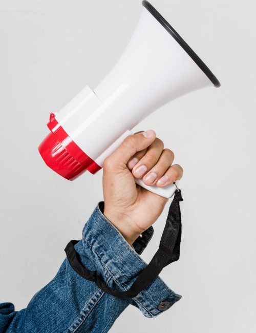 A person in a denim jacket holds a red and white megaphone, emphasizing communication.