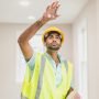 pexels-photo-8293645-8293645 A construction worker inspecting a room while wearing a hardhat and safety vest indoors.